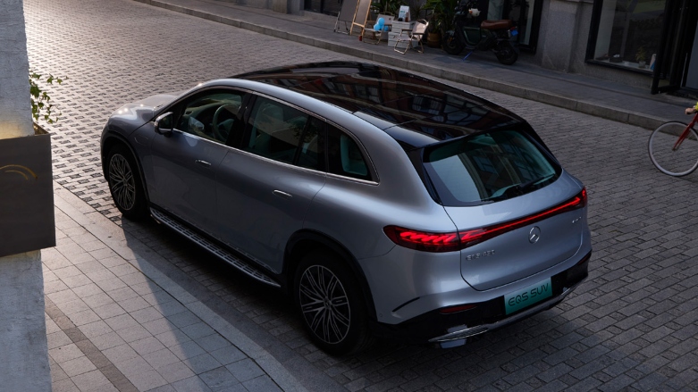 Vista lateral trasera de Mercedes Benz EQS color gris con muestra de techo panorámico estacionada en la ciudad.