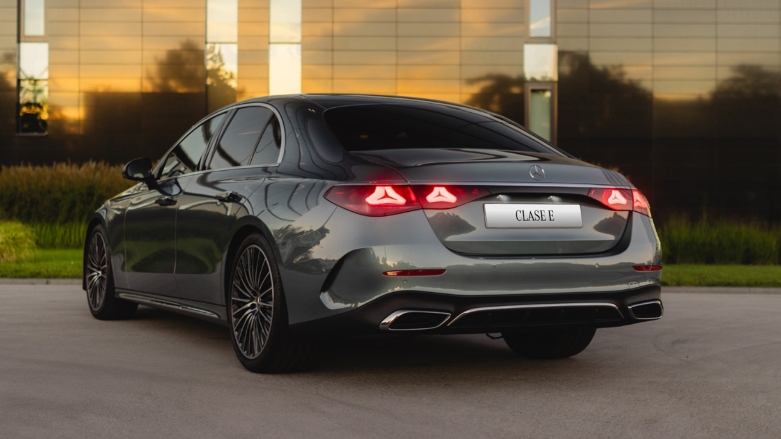 Vista trasera de Mercedes-Benz Clase E Sedán color gris estacionado en parqueadero con atardecer de fondo.
