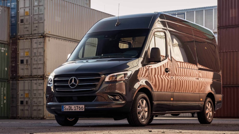 <p>Van de lujo Mercedes-Benz Sprinter de pasajeros color negra estacionada en zona de carga con contenedores alrededor.</p>